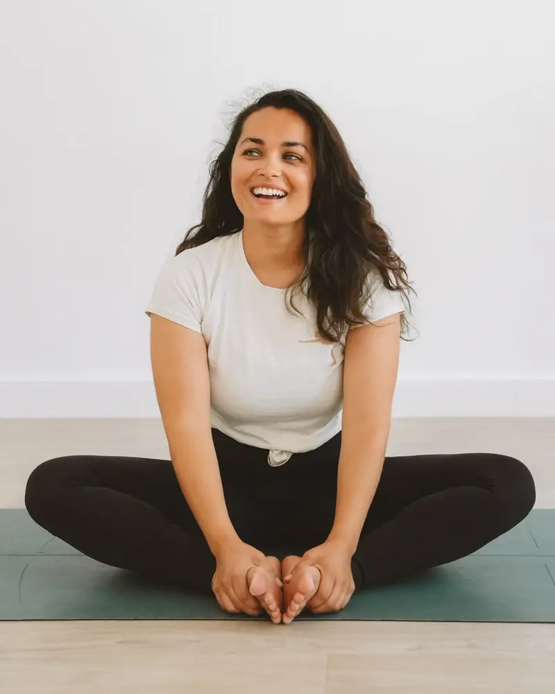 Delfine, assise en tailleur sur un tapis de yoga, sourit
